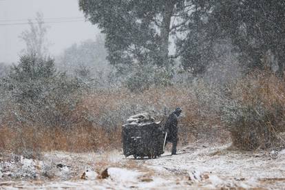A garbage collector moves a trash bin amid snowfall in Brackenhurst