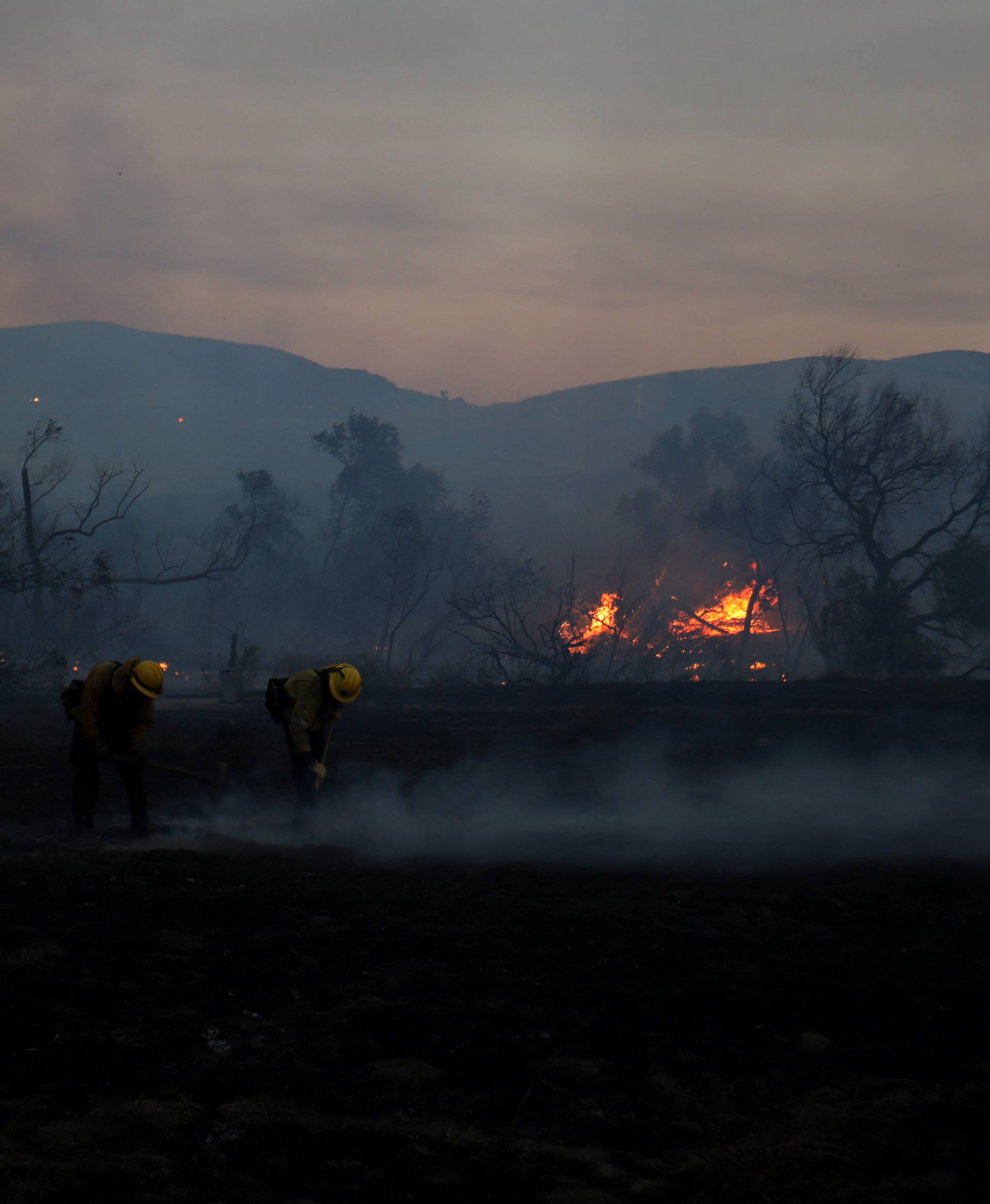 Firefighters work to put out hot spots on a fast moving wind driven wildfire in Orange, California