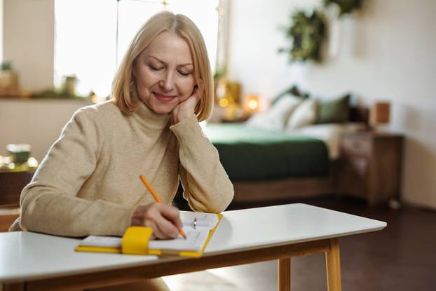 Mature,Woman,Writes,In,Her,Diary,Sitting,At,A,Desk