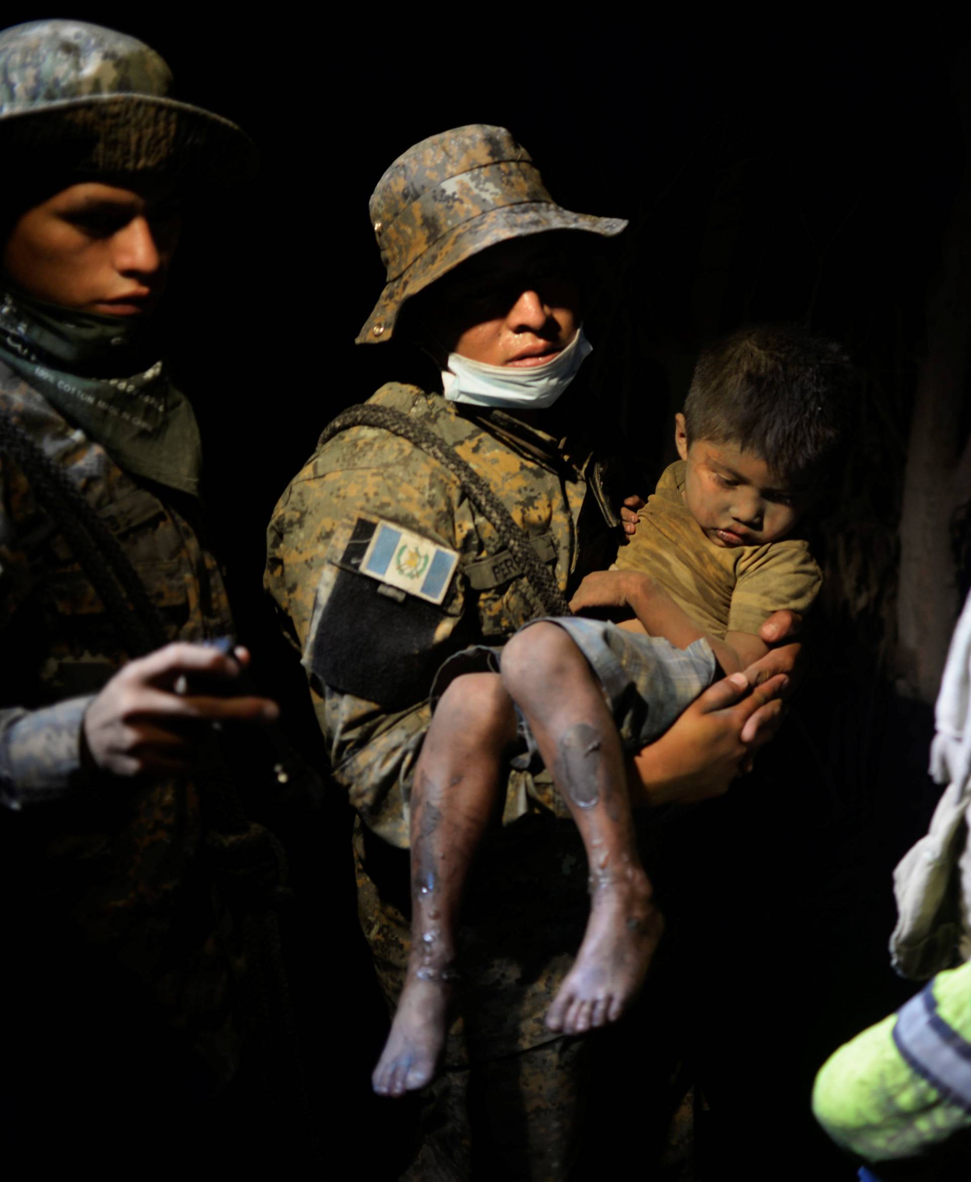 A soldier takes a rescued child covered with ash to a hospital after Fuego volcano erupted violently in El Rodeo
