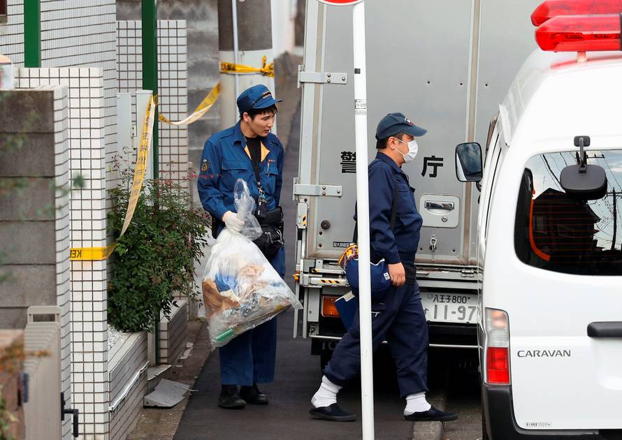 Police officer carries out a plastic bag from an apartment building where media reported nine bodies were found in Zama
