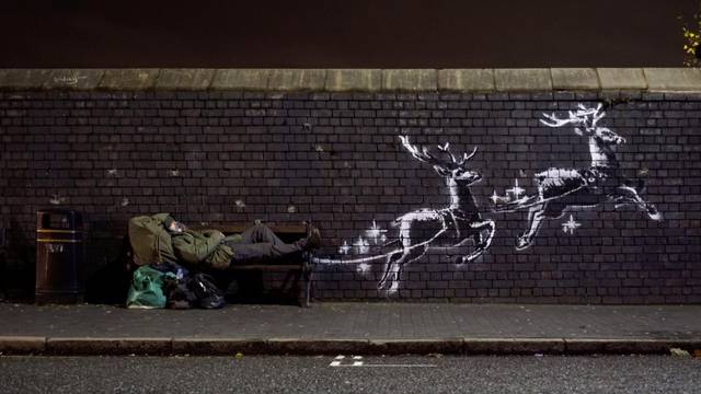 A man lays on a bench next to a new mural by Banksy in Birmingham