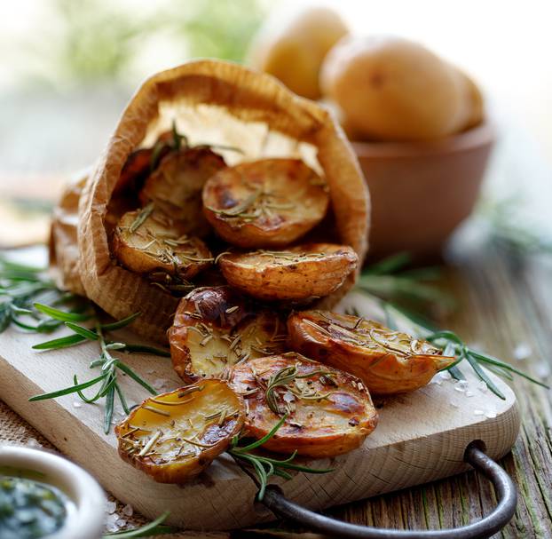 Baked potatoes. Baked halves of potatoes seasoned with rosemary and sea salt on a wooden rustic table.