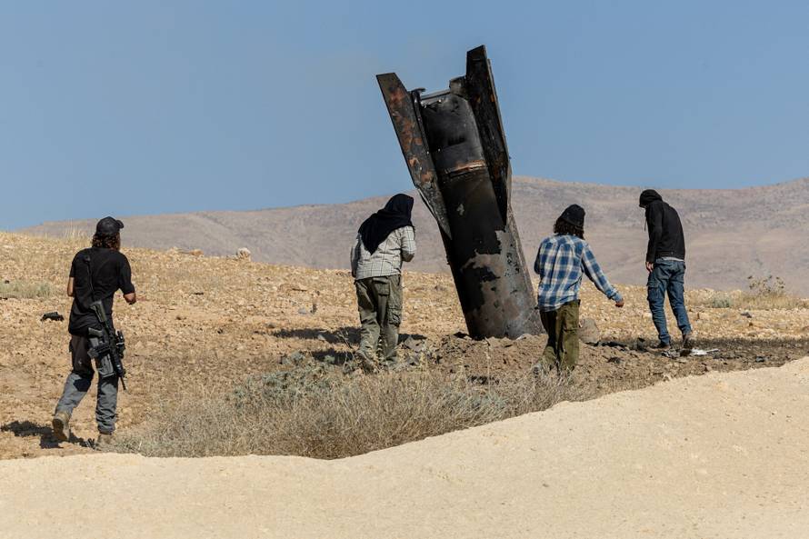 Israeli settlers stand next to part of a missile protruding from the ground, following strikes from Iran, in the central Israeli-occupied West Bank
