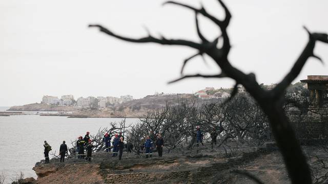 Firefighters look for missing persons after following a wildfire at the village of Mati, near Athens