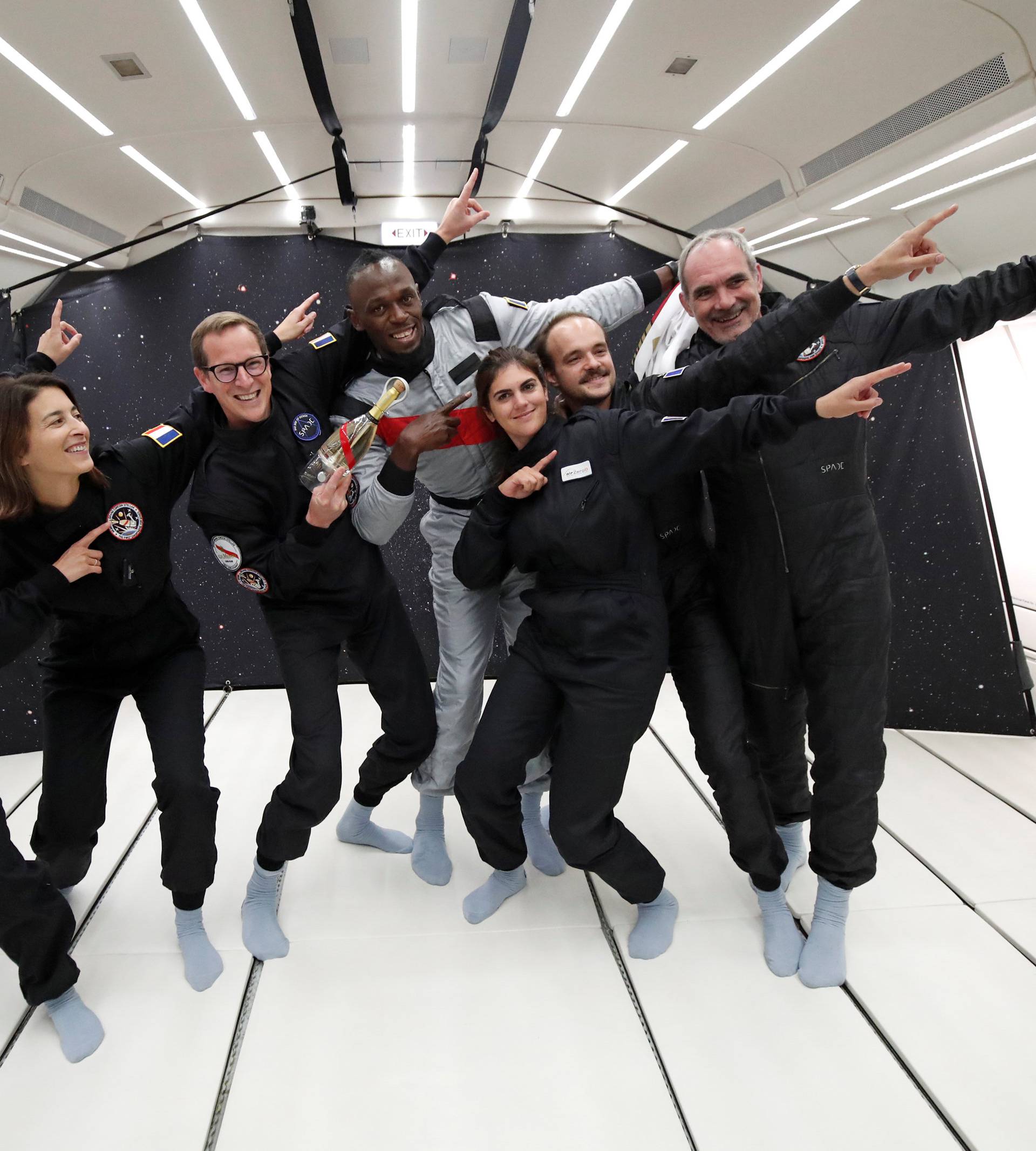 Retired sprinter Usain Bolt poses with staff members holding a bottle of "Mumm Grand Cordon Stellar" champagne after they enjoy zero gravity conditions during a flight in a specially modified Airbus Zero-G plane above Reims