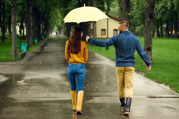 Love couple with umbrella hugs in park, back view