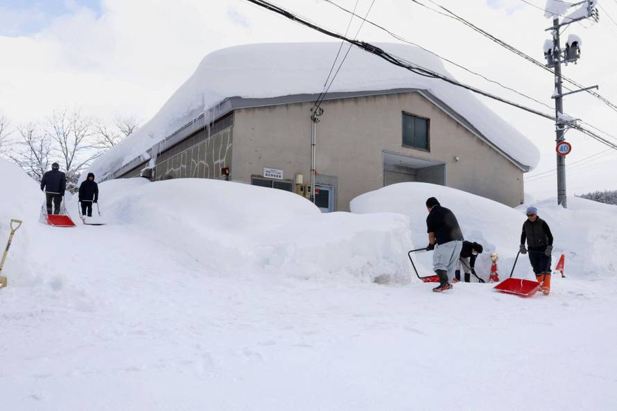 People remove snow near a house in Aomori, northeastern Japan, as heavy snow continues to hit the region