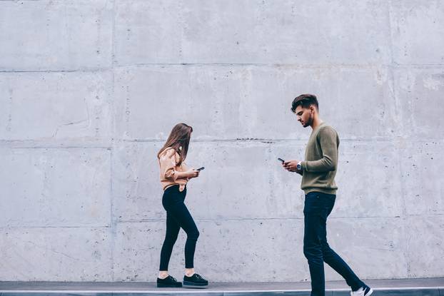 Male,And,Female,Hipsters,Walking,Outdoors,Looking,At,Their,Smartphones