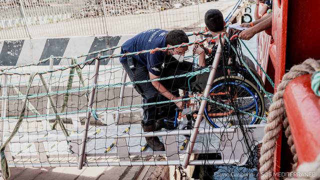 A migrant on a wheelchair is helped as he disembarks "Ocean Viking" ship, in Augusta