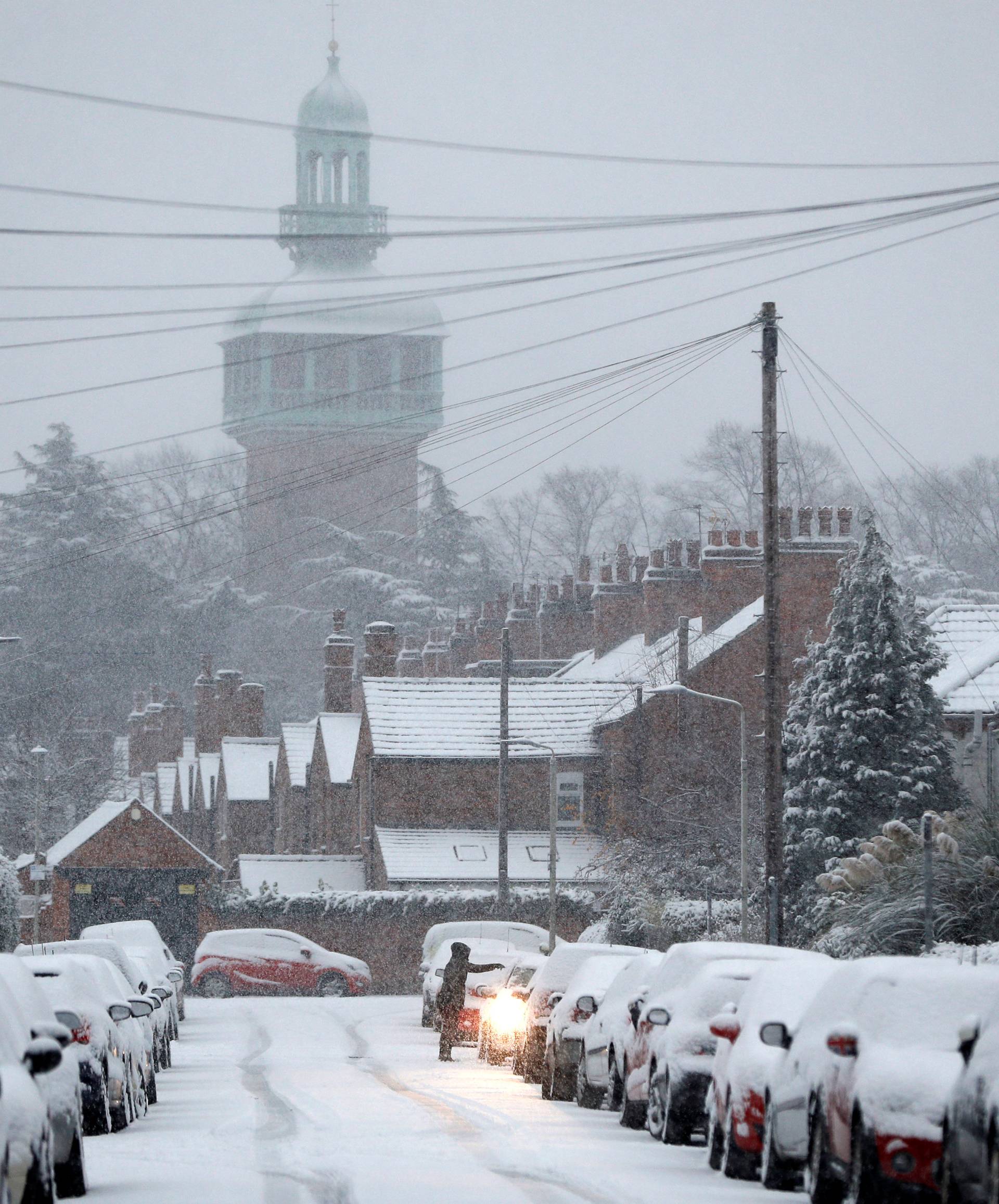 A resident clears snow from a car as the snow falls in Loughborough