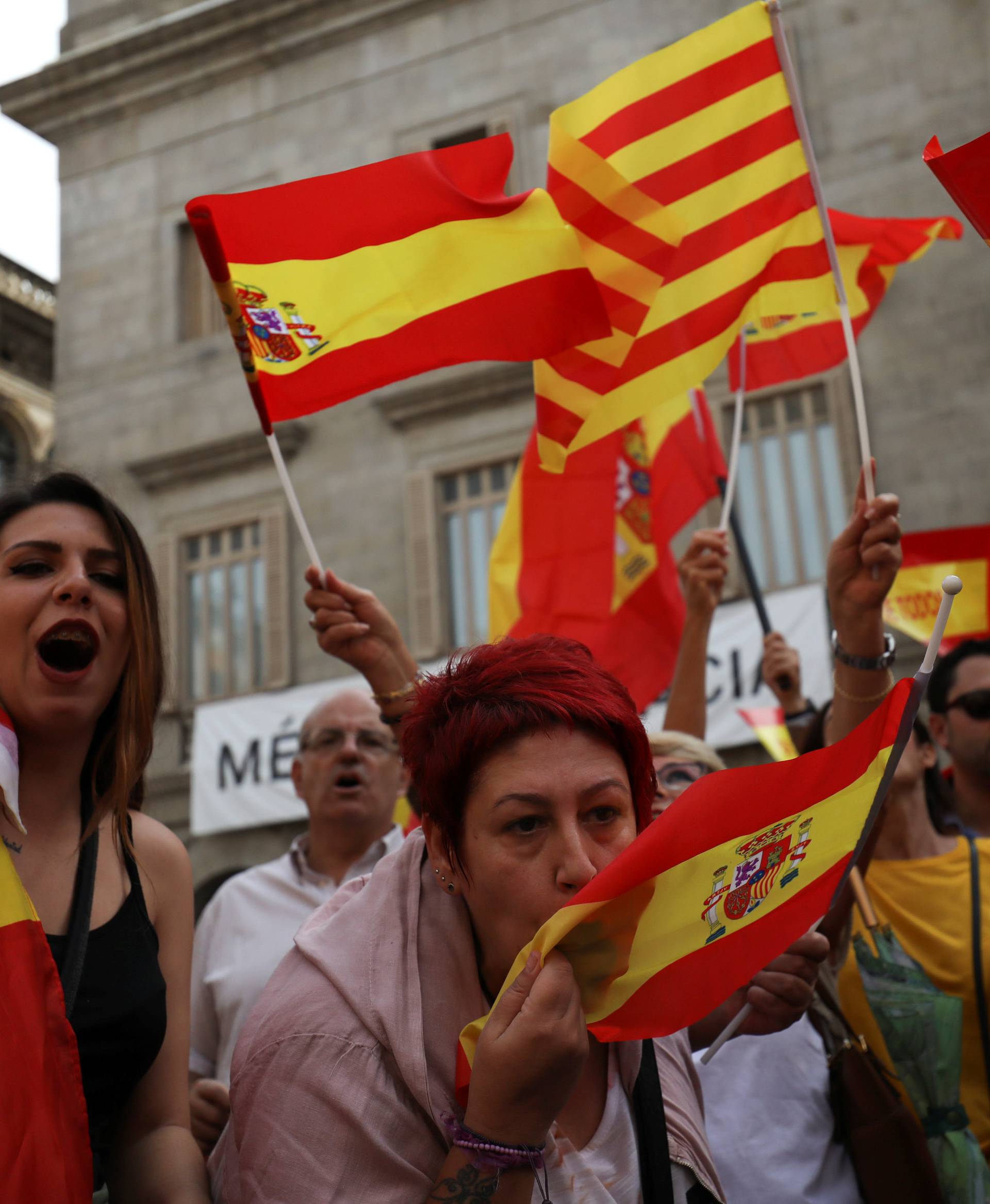 A woman kisses a Spanish flag as protesters hold Spanish and Catalan flags during a demonstration in favor of a unified Spain a day before the banned October 1 independence referendum, in Barcelona