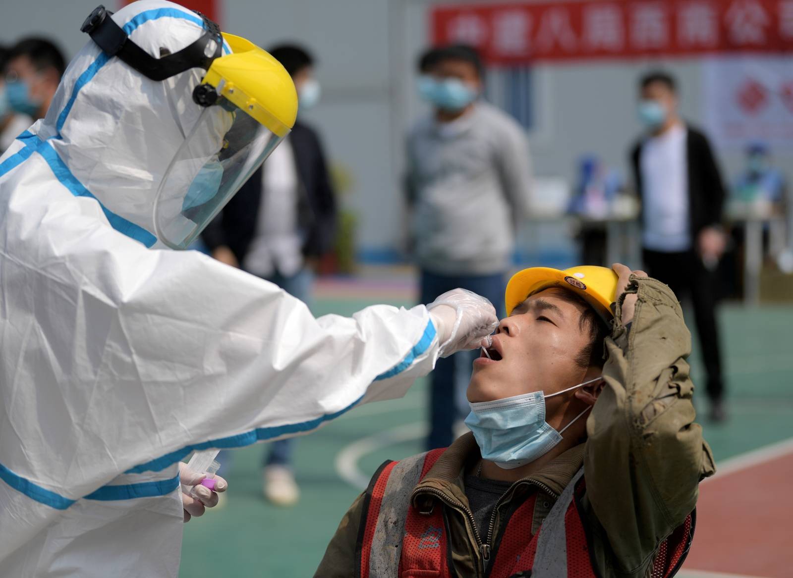 FILE PHOTO: Worker in protective suit collects a swab from a construction worker for nucleic acid test in Wuhan