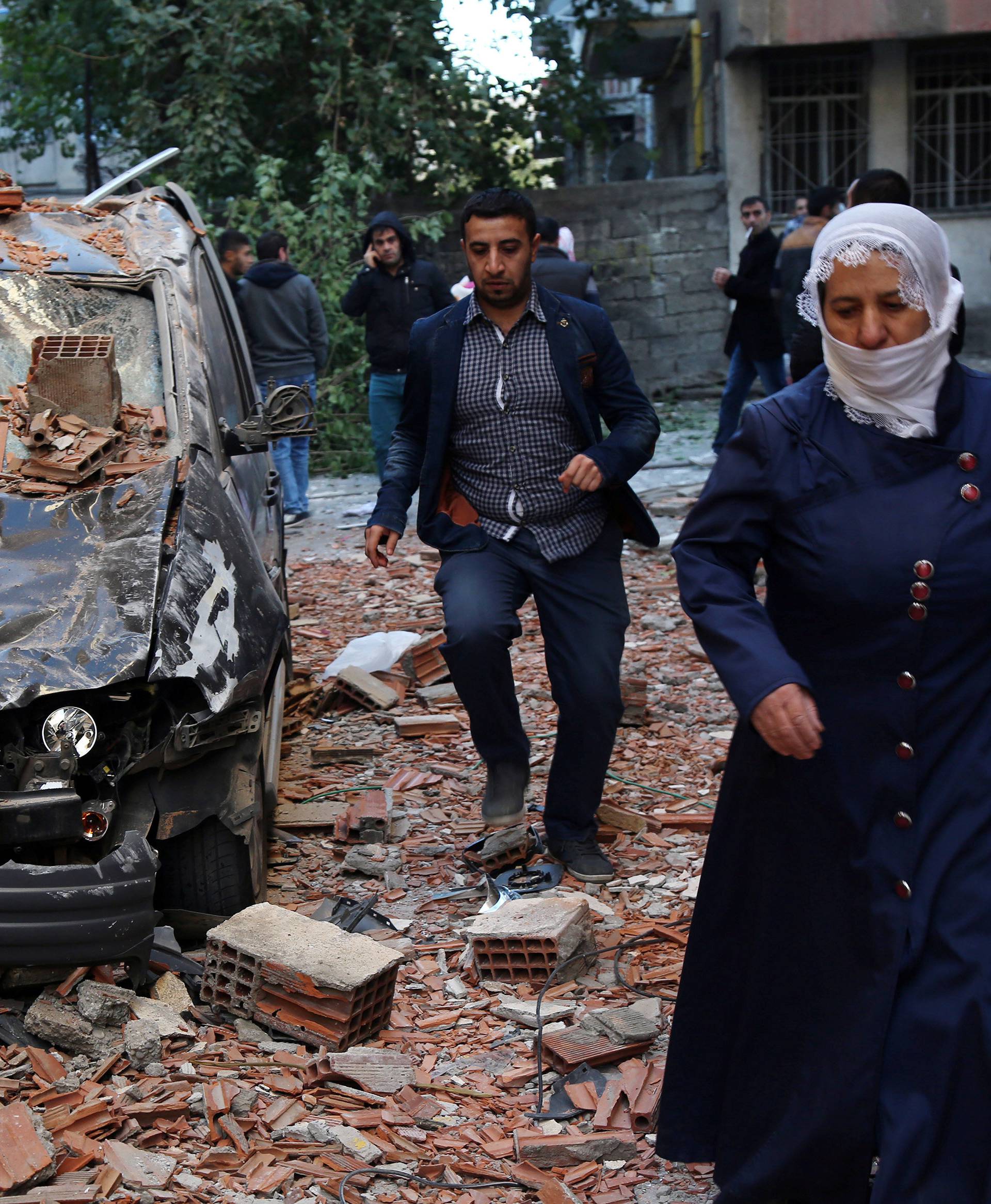 People walk past a damaged car after a blast in the Kurdish-dominated southeastern city of Diyarbakir