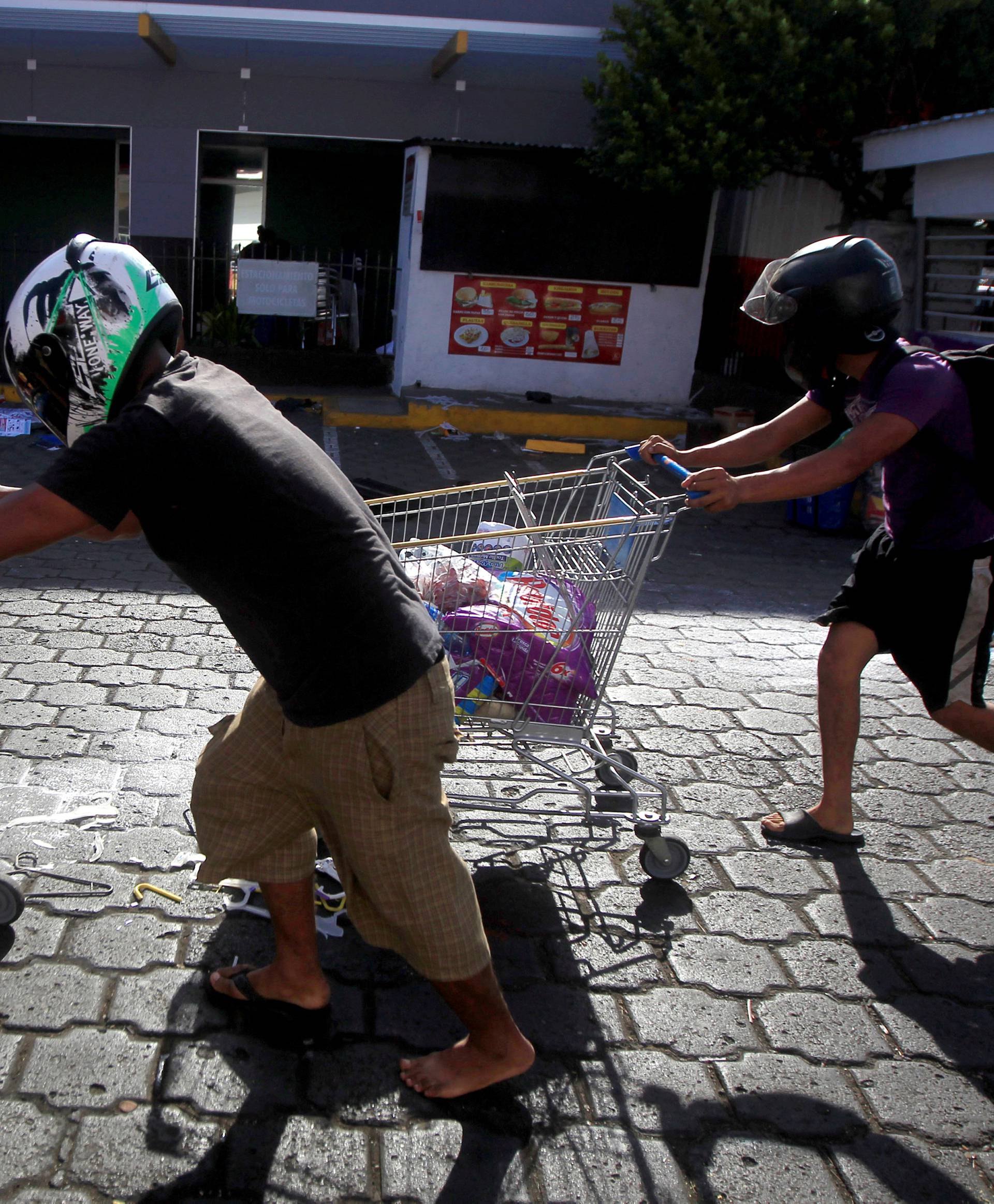 People with goods looted from a store push shopping trolleys along a street after protests in Managua