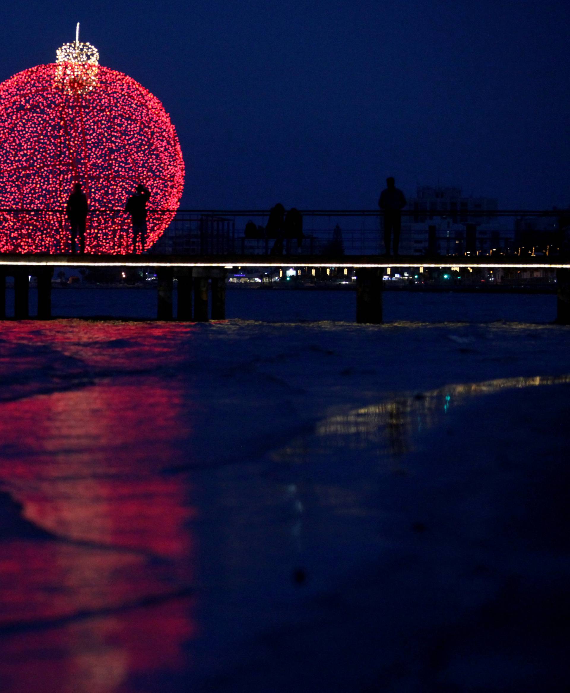 People are seen on a pier in front of a giant illuminated Christmas ball in Larnaca