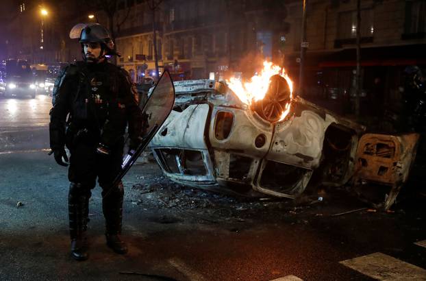 French riot police stand near an overturned burning car on avenue Kleber after clashes with protesters wearing yellow vests, a symbol of a French drivers