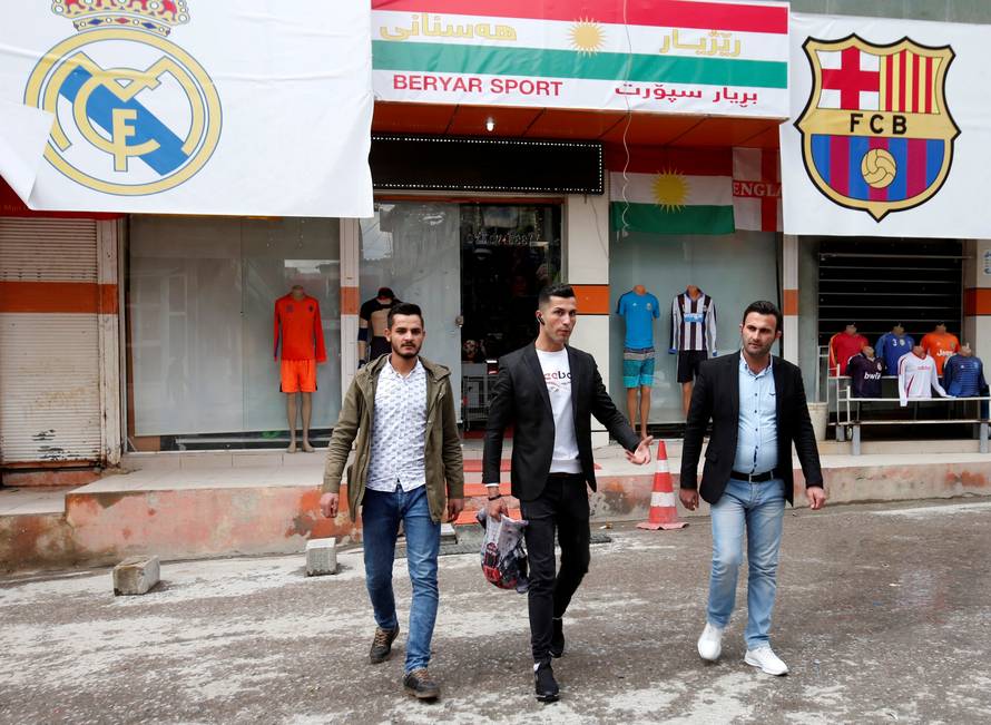 Biwar Abdullah, 25, an Iraqi Kurdish local footballer, who looks like the football player Cristiano Ronaldo, walks with his friends near a sportswear shop in the district of Soran, northeast of Erbil