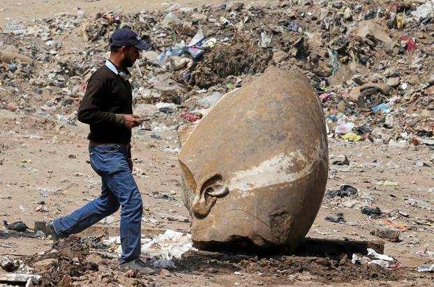 A man passes by what appears to be the head of an unearthed statue that workers say depicts Pharaoh Ramses II, in Cairo
