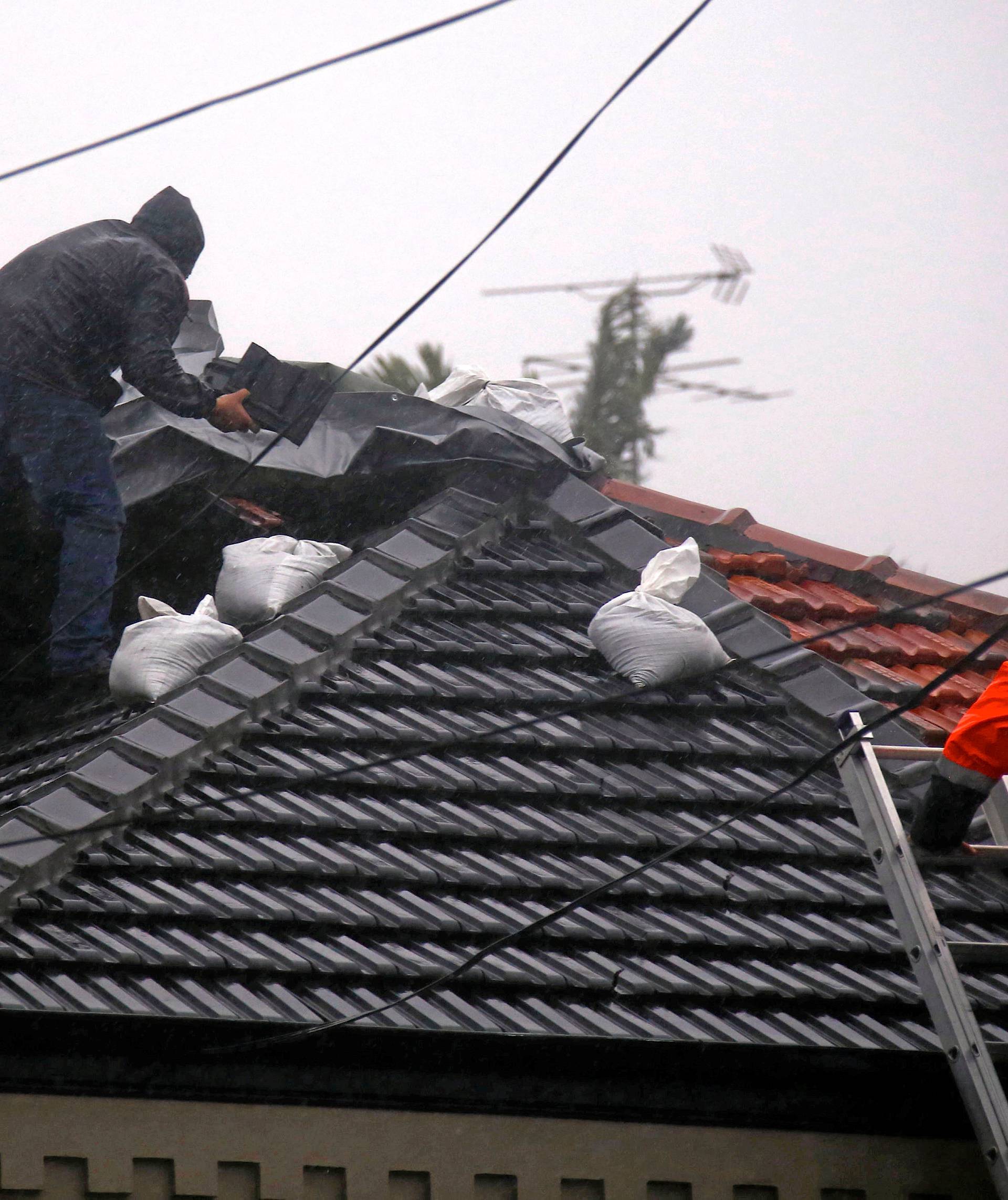 Two men work on covering damaged roof on house in severe weather  near Coogee Beach in Sydney