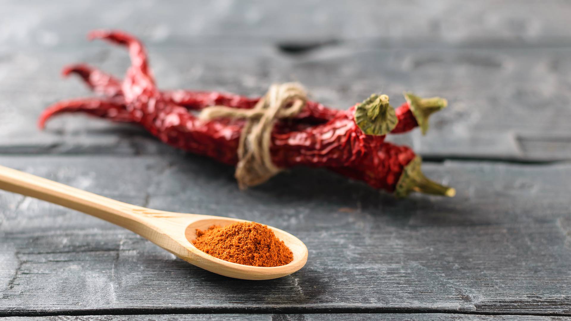 A light wooden spoon with ground pepper and a bunch of chili pods on the rustic table.