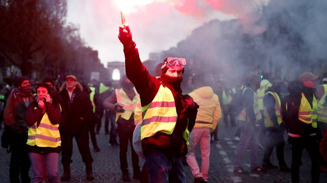 A protester wearing yellow vest, a symbol of a French drivers' protest against higher fuel prices, burns flare on the the Champs-Elysee in Paris