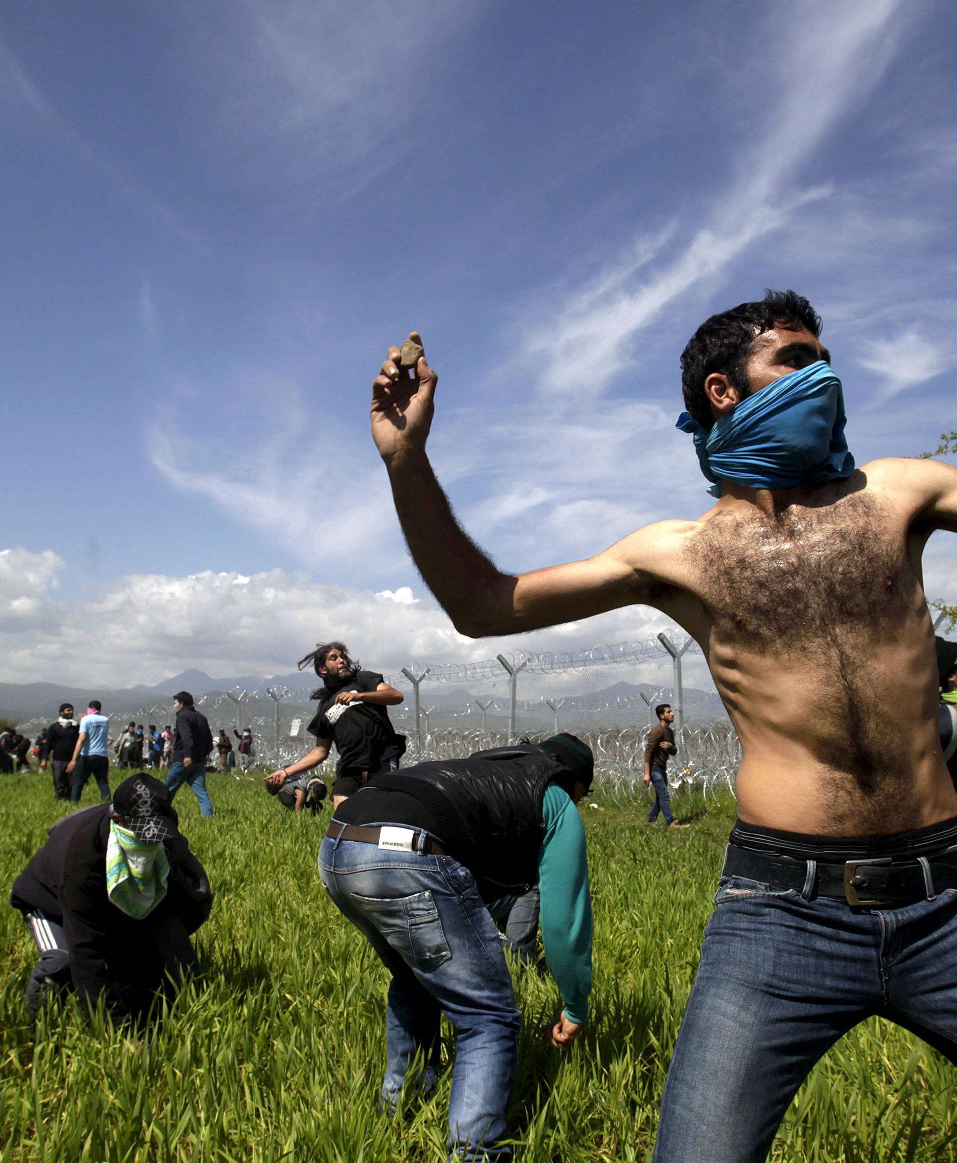 Migrants throw stones at Macedonian police during clashes next to a border fence at a makeshift camp for refugees and migrants at the Greek-Macedonian border near the village of Idomeni