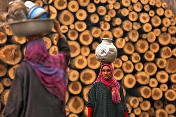 A woman carrying a metal pitcher filled with drinking water looks on in the outskirts of Srinagar