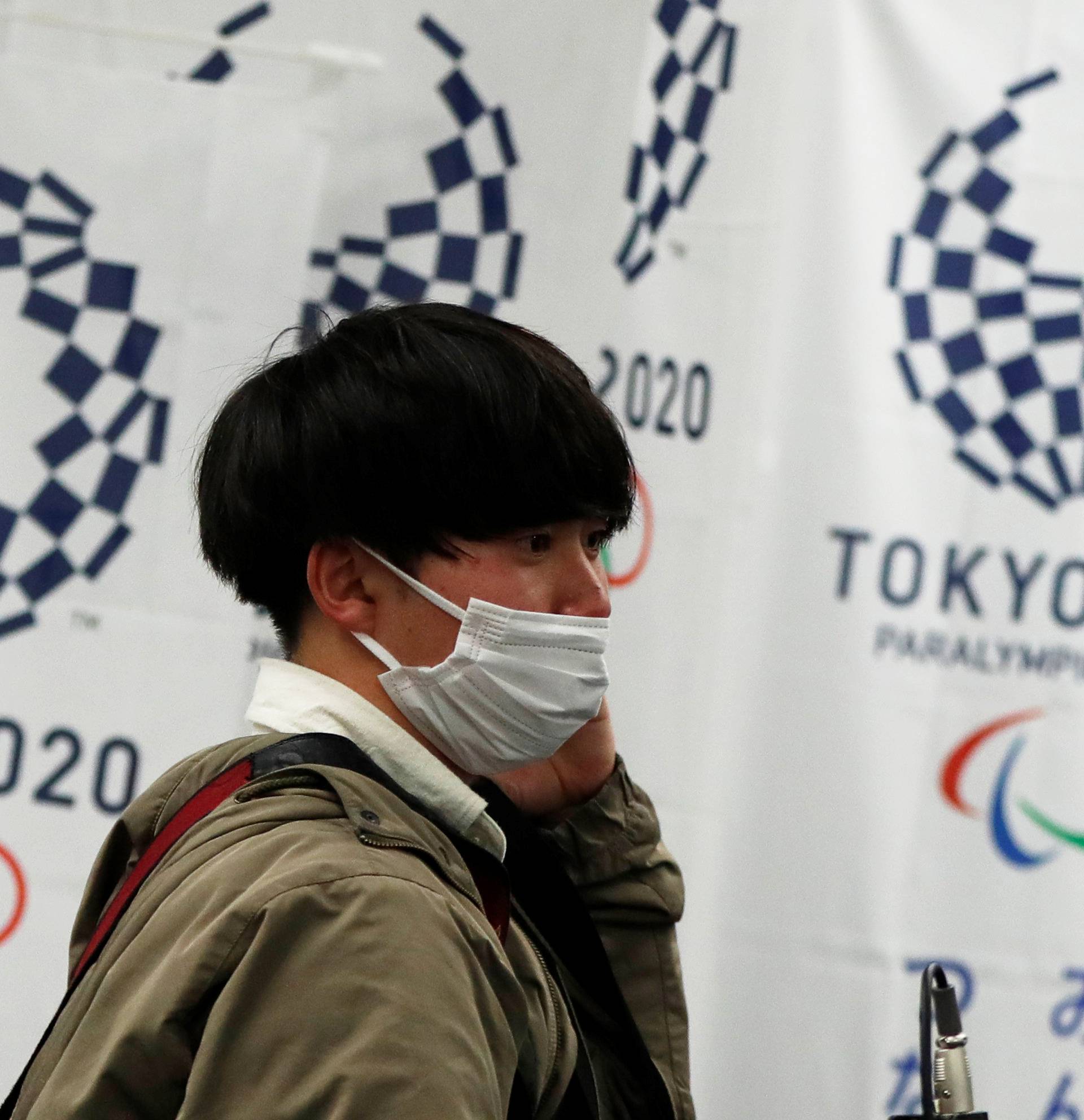 A man wearing a protective face mask, following an outbreak of the coronavirus disease (COVID-19), walks in front of flags of the Tokyo 2020 Olympic and Paralympic Games in Tokyo