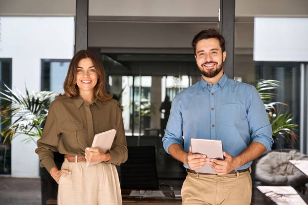 Two,Business,Partners,Executives,Standing,In,Office,Looking,At,Camera.