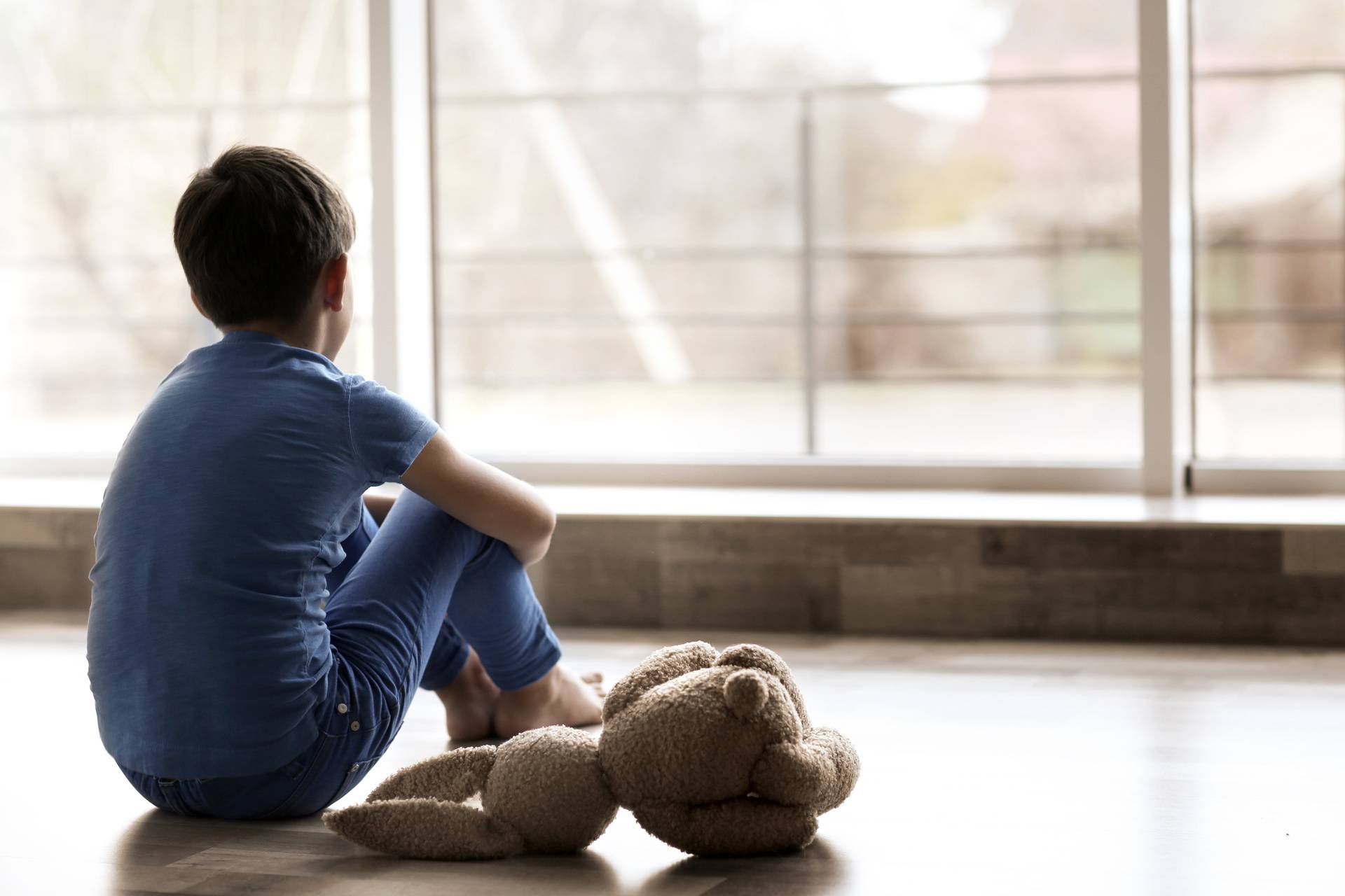 Sad little boy sitting on floor beside window