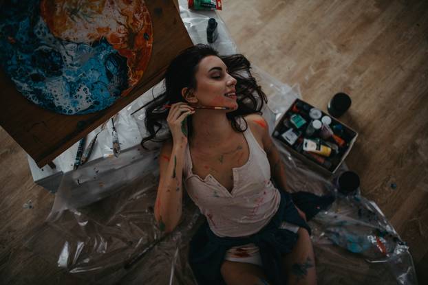 The artist sits on floor in an art workshop in a creative mess.