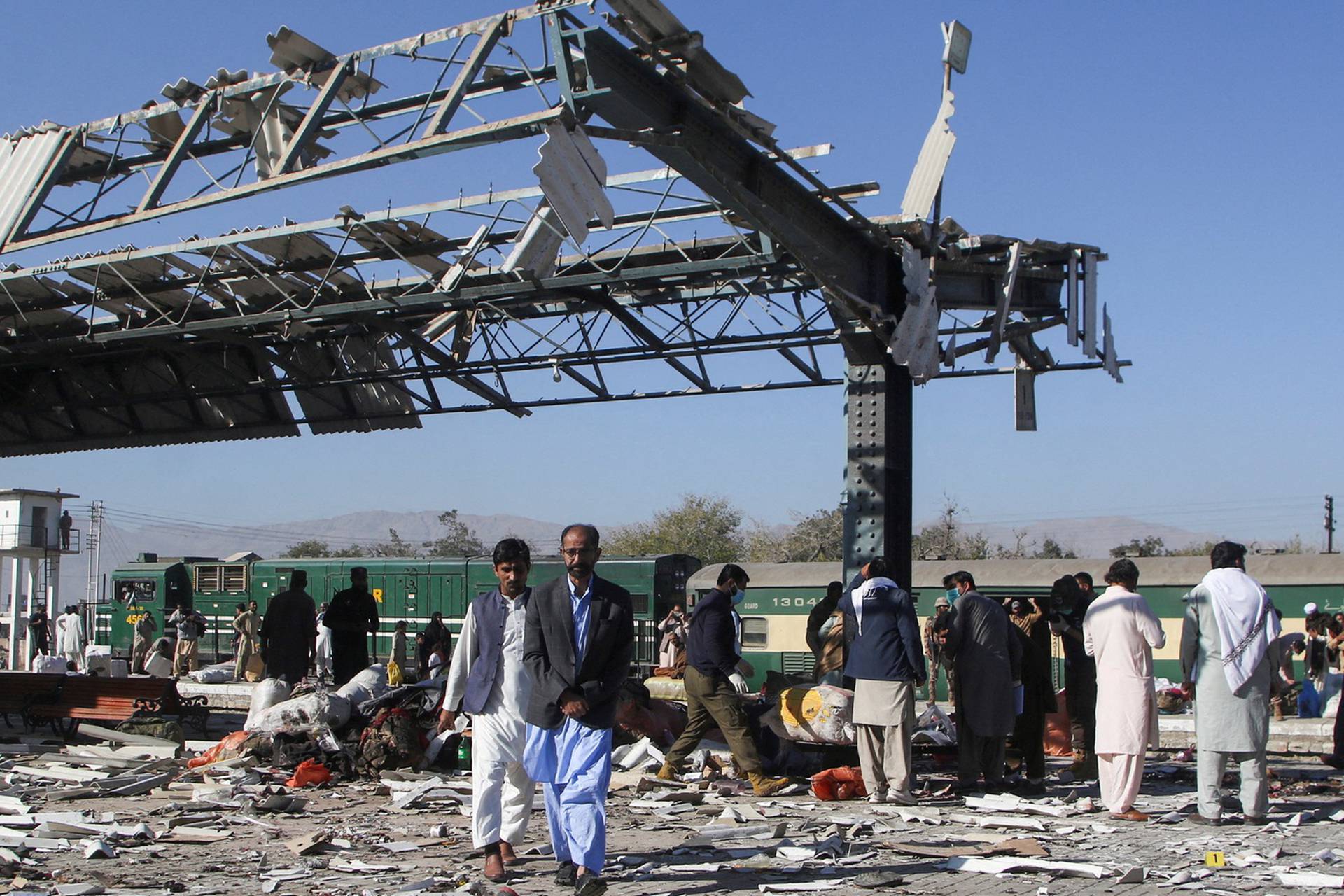 People walk amid debris after a bomb blast at a railway station in Quetta