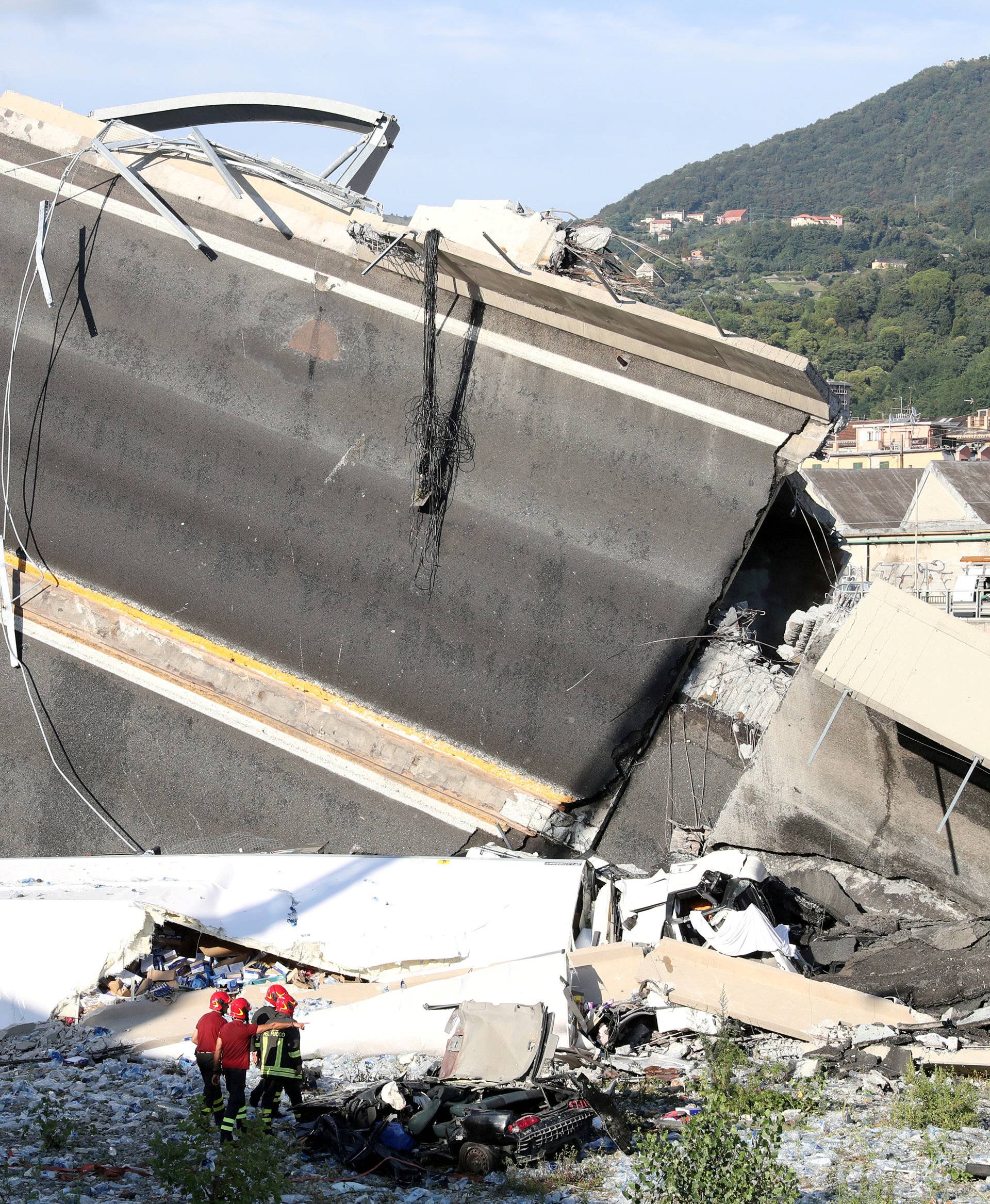 Firefighters and rescue workers stand next to collapsed motorway part at Morandi Bridge site in Genoa