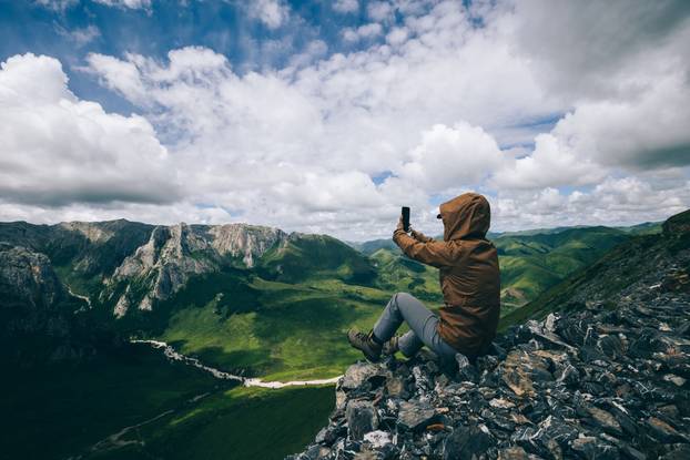 Successful woman hiker using smart phone on alpine mountain top