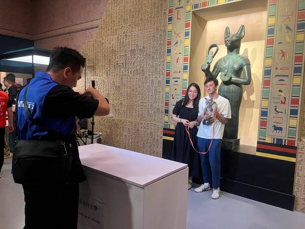 A cat and its owners pose for a photograph in front of a statue depicting the cat goddess Bastet at Shanghai Museum's "Meow Night\