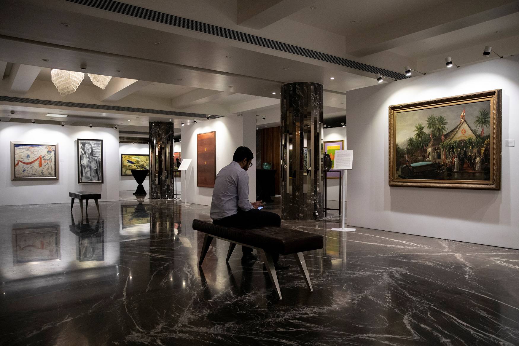 A staff member looks at his phone as artworks once part of billionaire jeweller Nirav Modi's collection are seen on display ahead of their auction at a gallery in Mumbai