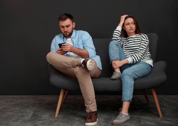 Young man preferring smartphone over his girlfriend at home. Rel