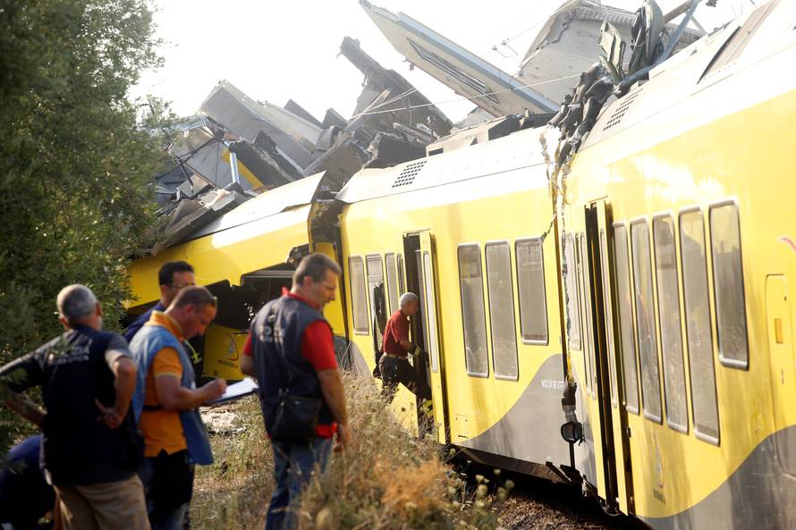 Rescuers stand at the site where two passenger trains collided in the middle of an olive grove in the southern village of Corato