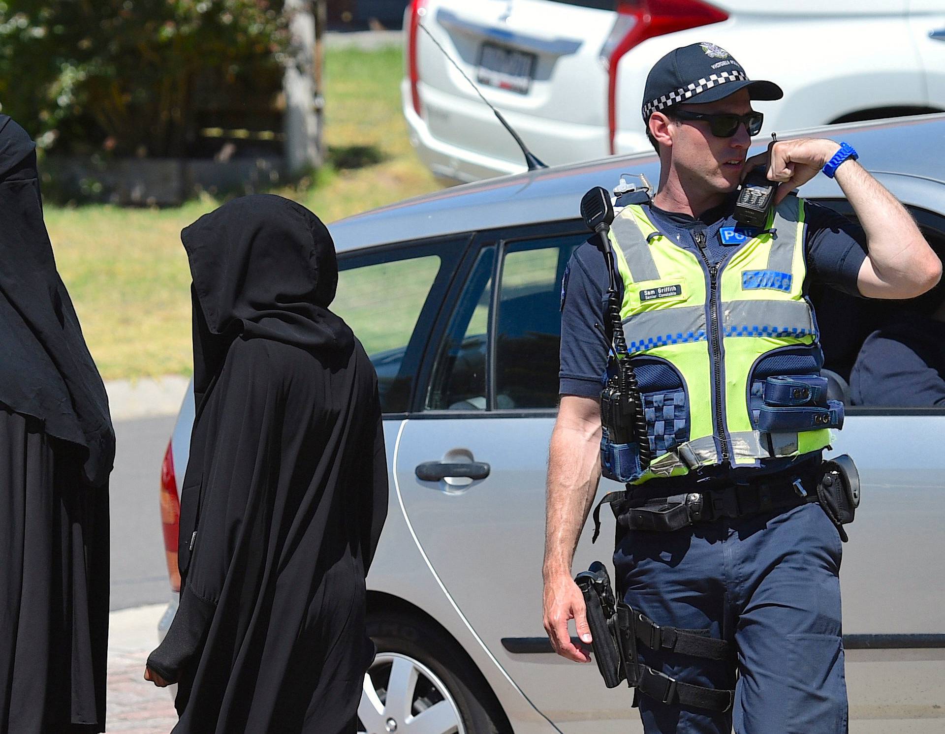 Women stand next to a policeman blocking a road where police officers are searching a house in the Melbourne suburb of Meadow Heights, Australia