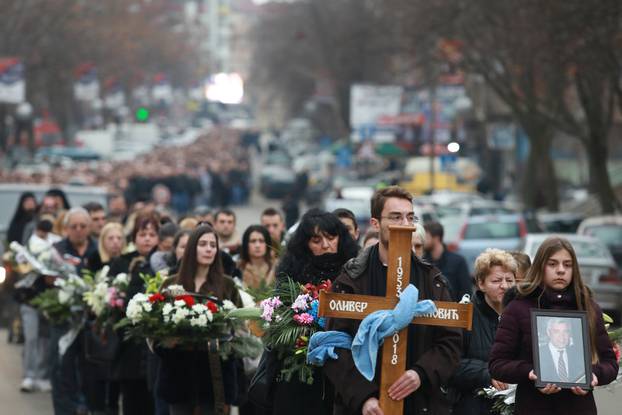 A cortege escorts a car carrying coffin of Oliver Ivanovic, flanked by priests and family,  to the northern outskirts of Kosovska Mitrovica