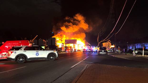 Smoke and flames rise from the site of a burning building, as emergency vehicles are parked nearby, in Denver