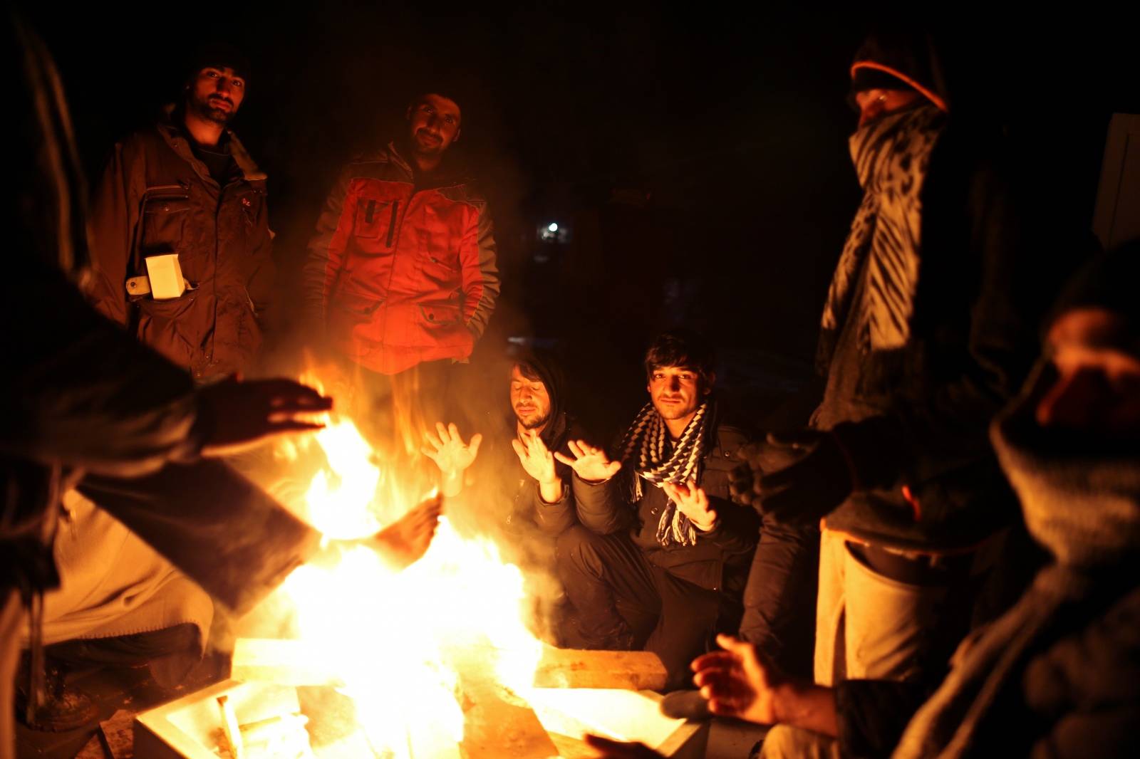 Migrants warm up around a fire at camp "Lipa" after it was closed, in Bihac