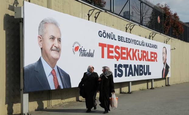 People walk past by AK Party billboards with pictures of Turkish President Erdogan and mayoral candidate Yildirim in Istanbul