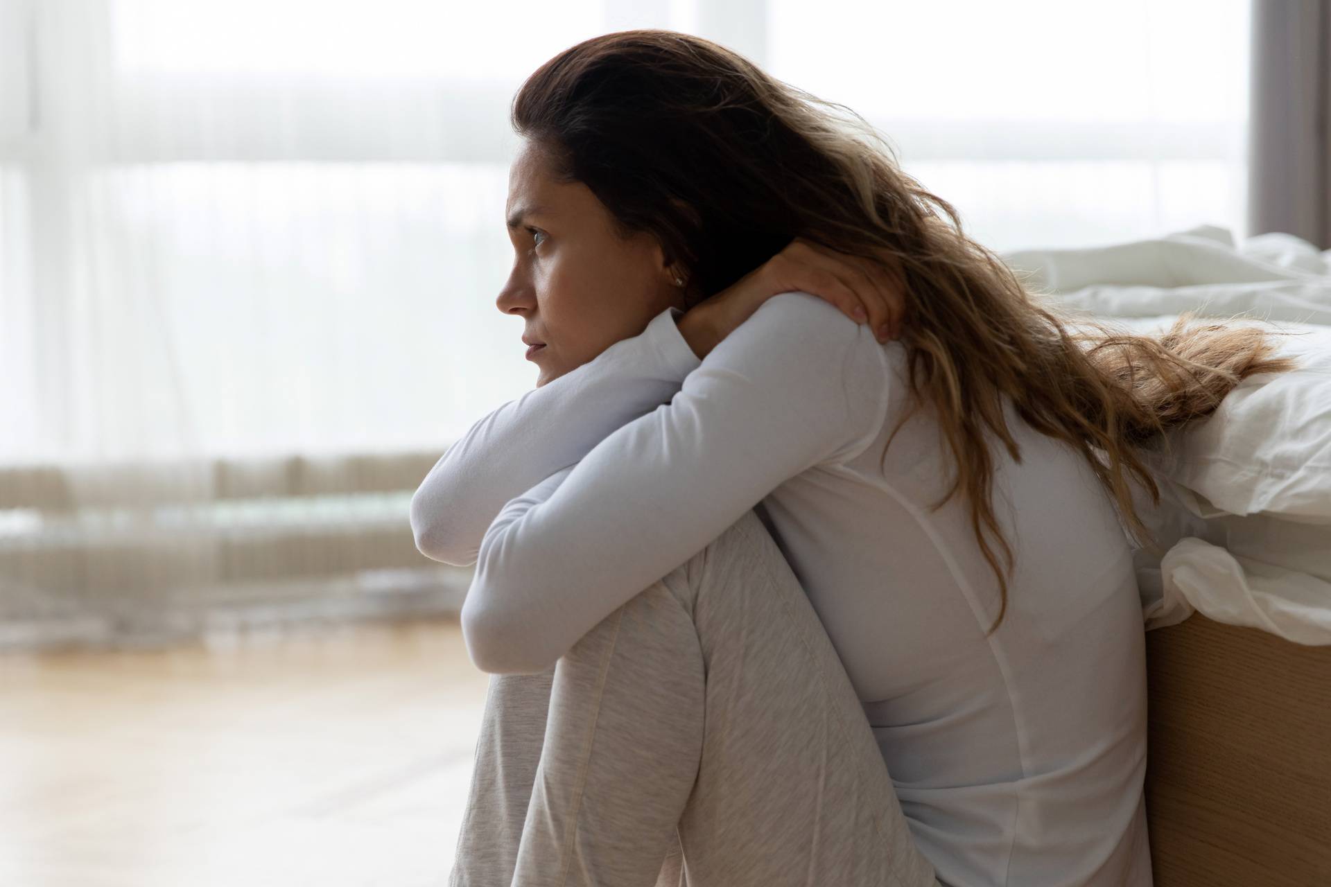 Sad woman sitting on floor leaned on bed feels lonely