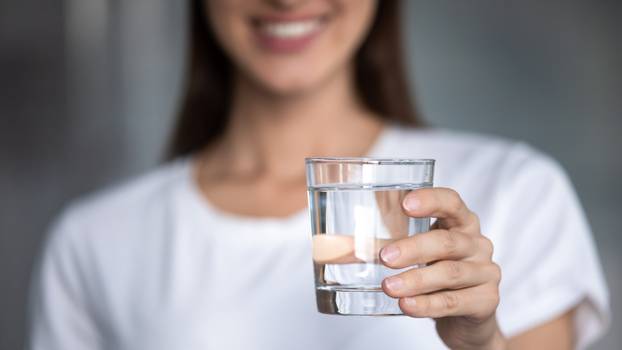 Closeup focus on female hand holding glass of clear water