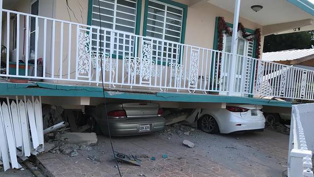 Cars lie under a collapsed house after an earthquake in Guanica
