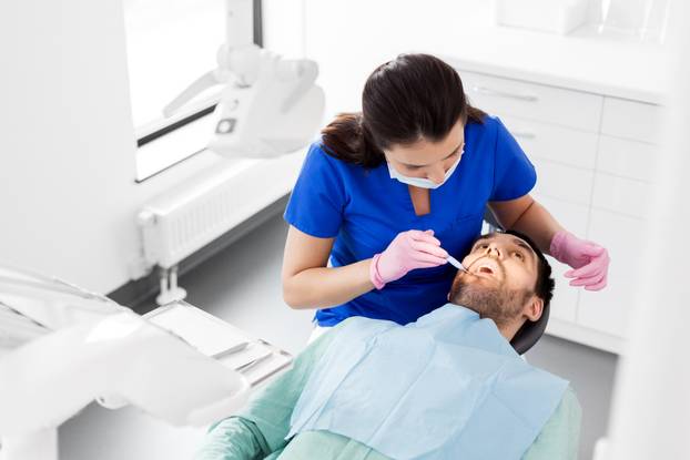 female dentist checking up male patient teeth