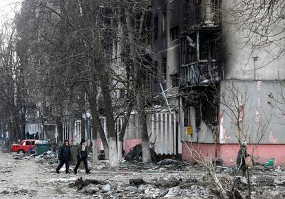 Local residents walk near a damaged residential building in the besieged city of Mariupol