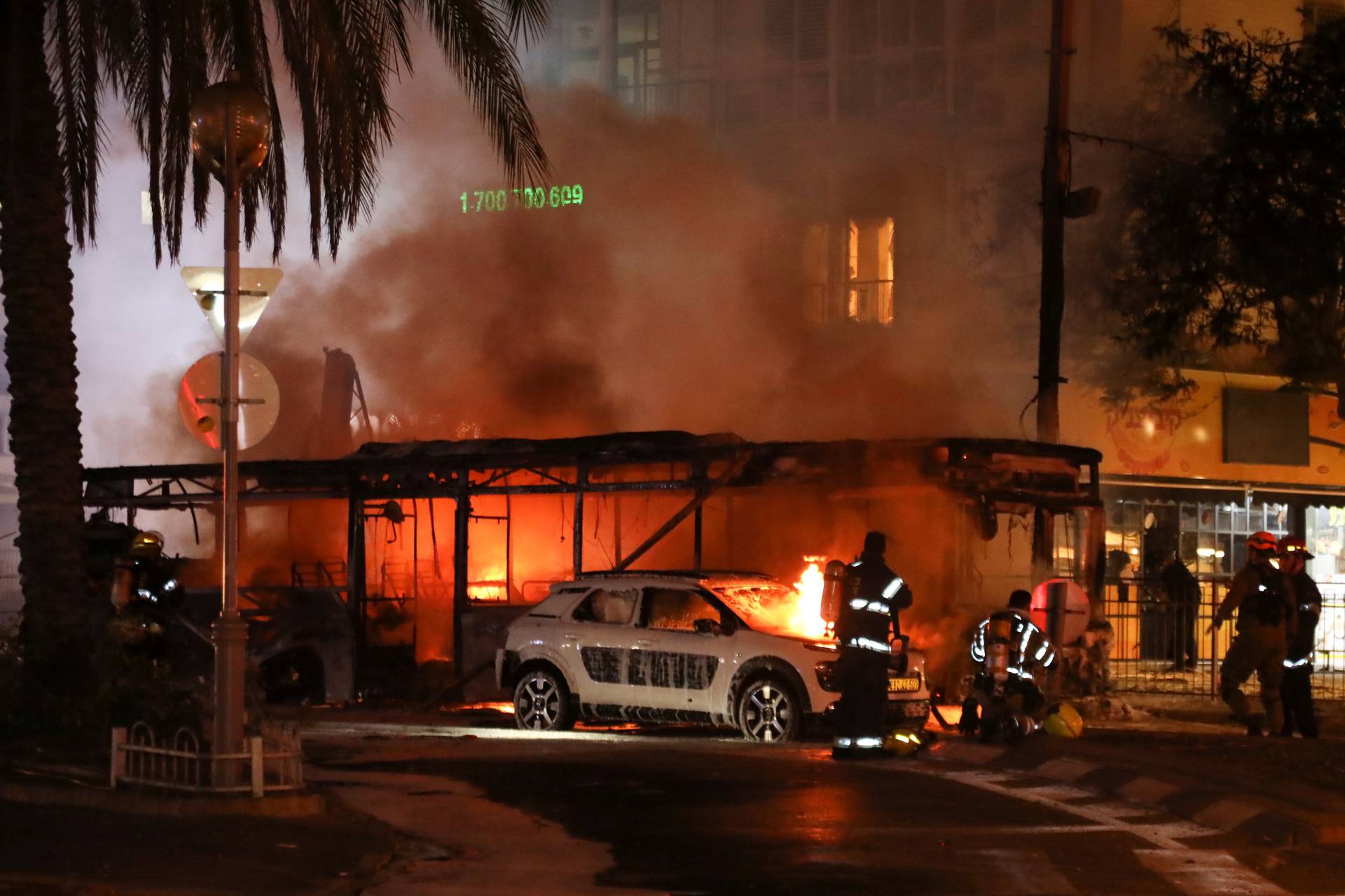 Israeli firefighters, security and rescue forces stand next to a burning bus and car that were hit by a rocket fired from Gaza towards Holon